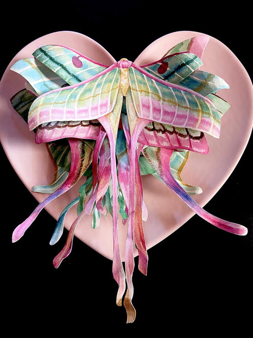 pink and green moths stacked on top of each other while sitting on a pink heart shaped plate. the moths match the shape.