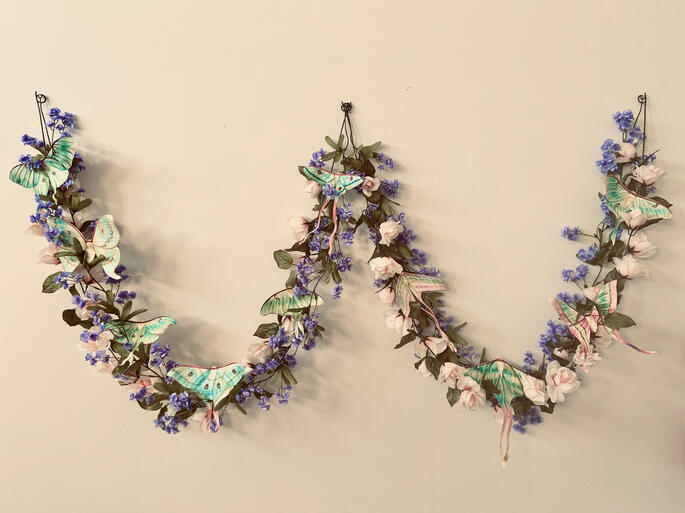 2 vines of flowers hanging loosely on a wall. there are many moths between their blooms.