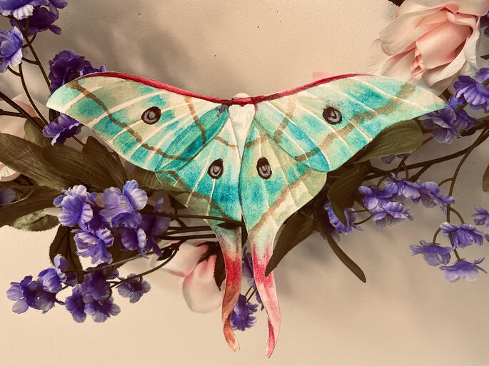 a teal moth on a vine of bright purple flowers and soft pink roses.